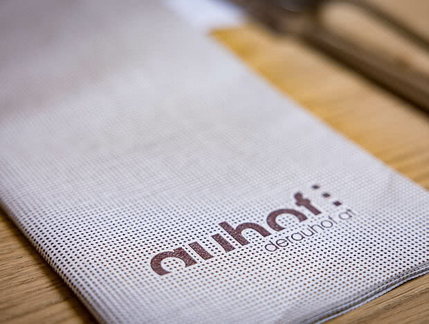 Nahaufnahme eines Stoffserviettenhalters im Gasthaus, bedruckt mit "Auhof" und der Website-Adresse