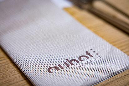 Nahaufnahme eines Stoffserviettenhalters im Gasthaus, bedruckt mit "Auhof" und der Website-Adresse