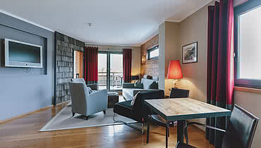 Geräumiger Wohnbereich mit Sitzgelegenheiten und Blick auf den Balkon im Hotel Auhof