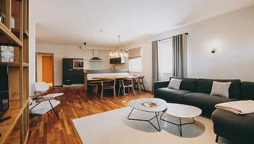 Auhof Hotel GmbH Helles Wohnzimmer mit grauem Sofa, runden Couchtischen und Blick auf die moderne Küche und den Esstisch